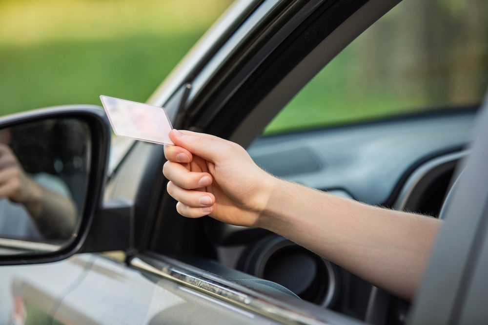 person hand out of the car window holding the driver license as shows it to the police officer for control